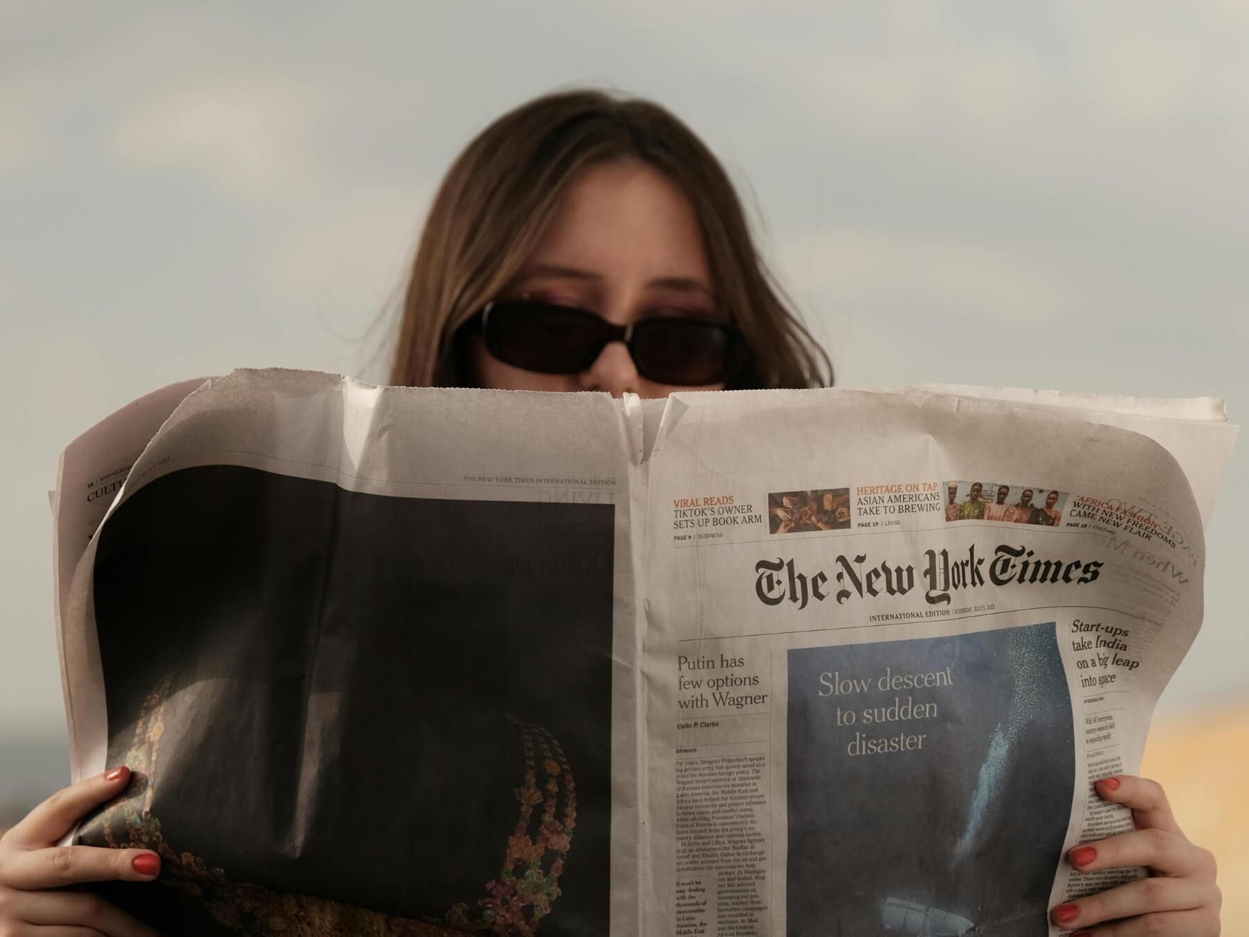 A woman sitting and reading the newspaper.